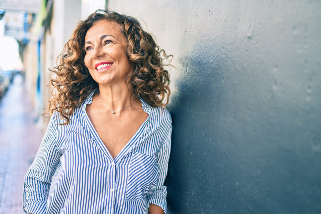 Middle age hispanic woman smiling happy leaning on the wall at the city.