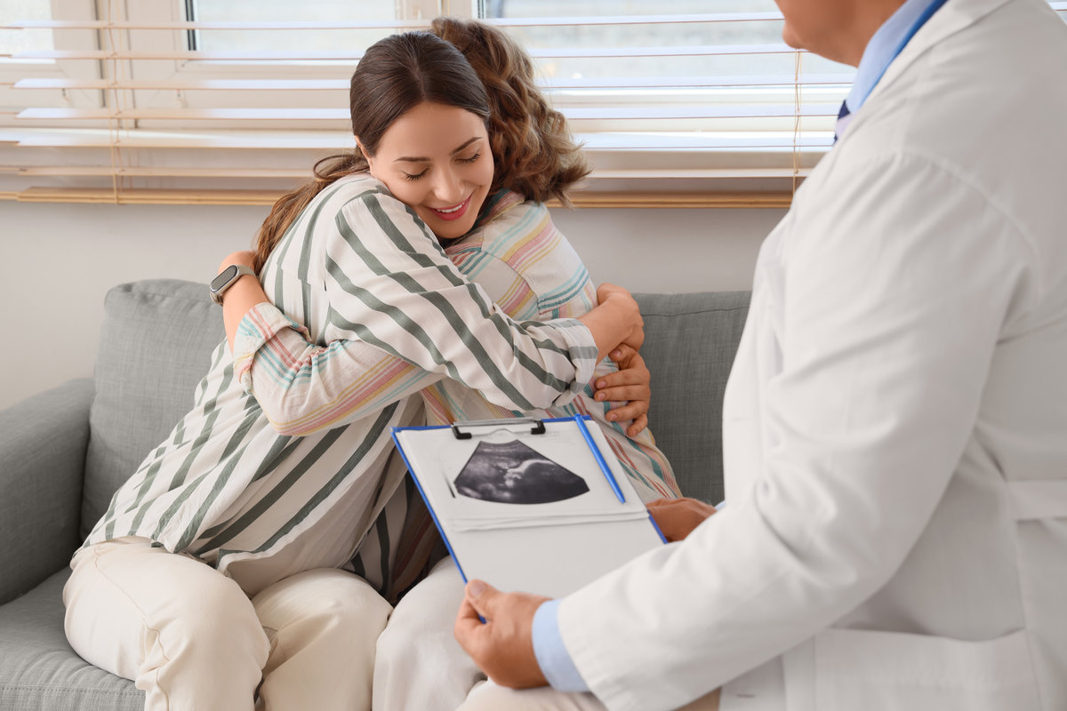 Young lesbian couple with fertility doctor hugging after IVF in clinic