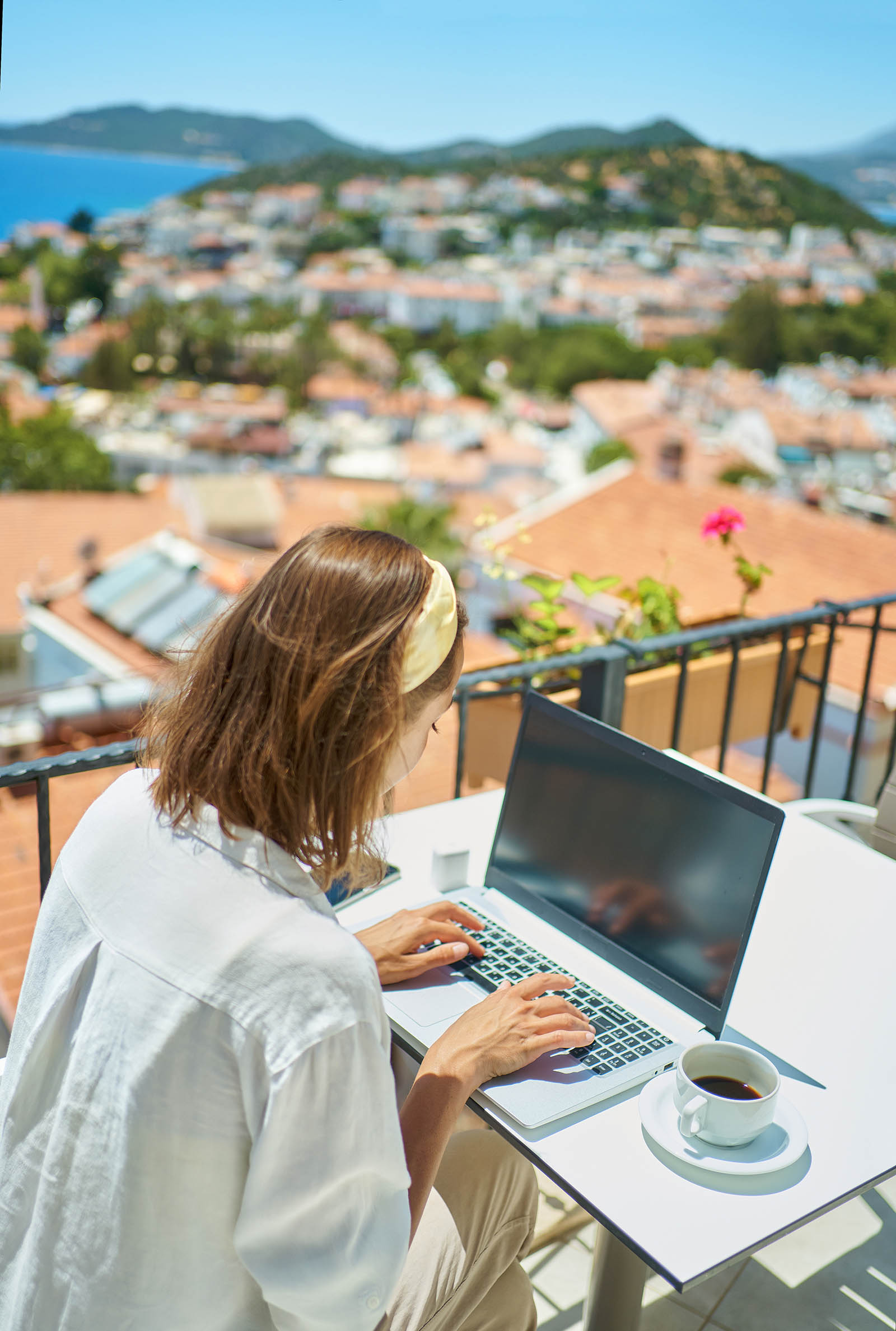 Woman working remotely on a laptop on a balcony overlooking a scenic view